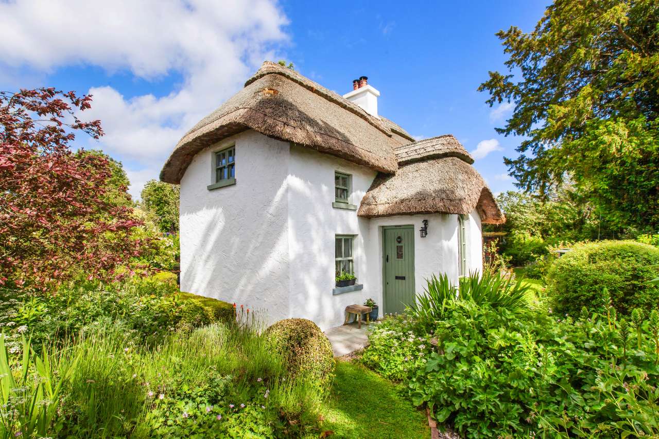 Genista Cottage exterior with thatched roof and red acer tree